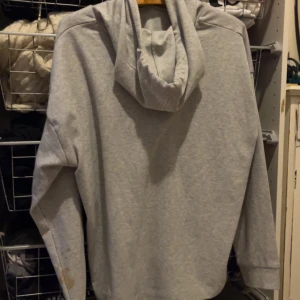 Grå hoodie med dragsko - Säljer en stilren grå hoodie med dragsko i huvan. Perfekt för en avslappnad look. Den har långa ärmar och en mjuk känsla.