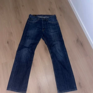 Blå jeans från Lee - Snygga blå jeans från Lee med klassisk femficksdesign och guldfärgade sömmar. De har en rak passform och är tillverkade i slitstarkt denim. Perfekta för en avslappnad stil.