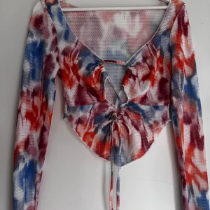 Färgglad långärmad topp med knytning - Säljer en färgglad långärmad topp med ett abstrakt mönster i blått, rött och orange.   Rensar ur min garderob just nu🌼 Kika och se om du ser något mer i min profil som du gillar så skickar jag med det till dig också!😊 Fler kläder kommer! 