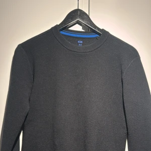 Svart stickad tröja från WE - Säljer en stilren svart stickad tröja från WE. Tröjan har en rund halsringning med en blå randdetalj på insidan av kragen. Perfekt för kyligare dagar.