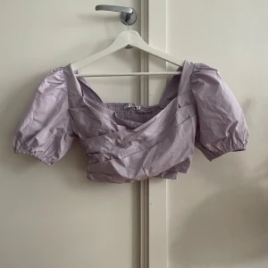 Ljuslila omlottopp i bomull  - Säljer en söt ljuslila omlottopp från Nakd. Den har korta puffärmar och en omlottdesign framtill. Endast provad men aldrig använd.