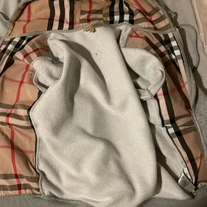 Burberry zip up  - Säljer en grå hoodie från Burberry med en klassisk rutig insida i beige, svart och röd. Jackan har dragkedja och snörning med metalländar. Perfekt för en stilren look.