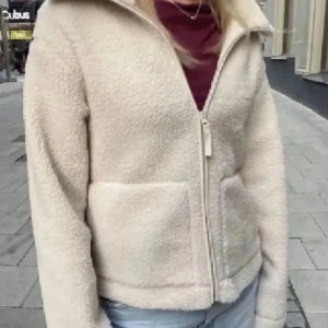 Beige teddyjacka med dragkedja - Mysig beige teddyjacka med dragkedja framtill. Jackan har en hög krage och två praktiska fickor. Perfekt för kyliga dagar när du vill hålla dig varm och bekväm. Köpt från H&M tror de är slutsålda på hemsidan och i de flesta butiker. 
