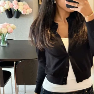 Svart cardigan  - Säljer en stilren svart kofta med knappar framtill. Perfekt för lager-på-lager och passar till många olika outfits. Koftan har långa ärmar och en klassisk design.