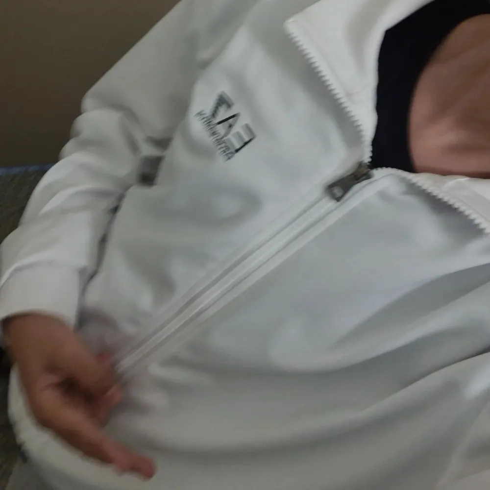 Säljer en stilren vit jacka från EA7 med dragkedja framtill. Jackan har en hög krage och långa ärmar, perfekt för en sportig look. EA7-loggan är tryckt på bröstet. Passar bra för både träning och vardag. ÄKTA!!! Storlek S. Neuletakit & Villapaidat.