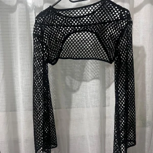 Svart nätmönstrad bolerotopp - Snygg svart bolerotopp i nätmönster med långärmad design. Perfekt för att lägga till en edgy touch till din outfit. Passar bra över en enkel topp eller klänning.