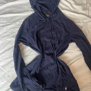 Mörkblå tunn hoodie från Ralph Lauren - Säljer en snygg mörkblå hoodie från Ralph Lauren med en liten broderad logga i vitt på framsidan. Tröjan har långa ärmar och en klassisk huva med dragsko. Perfekt för en avslappnad stil.