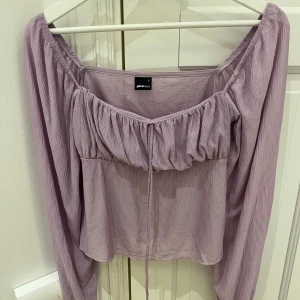 Lila blus från gina - Säljer en söt lila blus från gina med långa ärmar och en knytning framtill. Blusen har en lös passform och är perfekt för vår och sommar. Den har en lätt rynkad design vid bysten som ger en fin detalj.