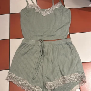 Grön ribbad linnetopp med spetsdetaljer - Säljer en söt grön pajamas med ribbad linnetopp och shorts med smala axelband och vacker spetskant i vitt. Perfekt för en avslappnad stil med en touch av elegans. Matchande shorts med knytband och spetsdetaljer ingår.