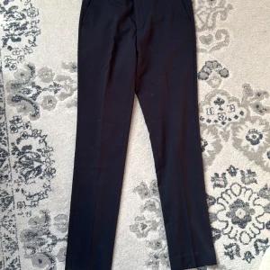 Mörkblå kostymbyxor från Jack & Jones - Snygga mörkblå  kostymbyxor från Jack & Jones. De har en klassisk rak passform med midwaist och är perfekta för en stilren look. Byxorna har diskreta fickor och hällor för bälte.