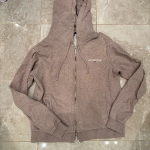 Beige hoodie från Lexington - Säljer en snygg beige hoodie från Lexington med dragkedja och huva. Tröjan har långa ärmar och ribbade muddar vid ärmslut och nederkant. Perfekt för en avslappnad stil.