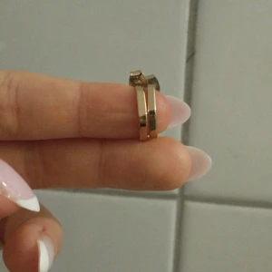 Guldiga örhängen i geometrisk design - Säljer ett par stilrena guldiga örhängen med en unik geometrisk form. De är små och eleganta, perfekta för både vardag och fest. Örhängena har en enkel stiftlåsning som gör dem lätta att bära. Passar perfekt för dig som gillar minimalistisk stil.