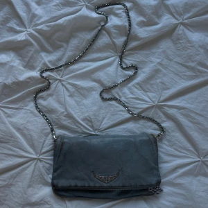 Grå Zadig & Voltaire väska med kedja - Säljer min ljusblå Zadig väska då den inte längre kommer till användning. Den har dock kommit till flitig användning varpå missfärgningen på baksidan haha! Skriv angående prutande🤗