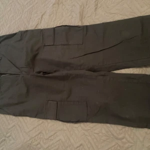 Svarta cargopants från Saligia - Säljer ett par svarta cargopants från Saligia i storlek 157. Byxorna har flera praktiska fickor och är perfekta för en avslappnad stil. De är i bra skick och passar till både vardag och äventyr. Perfekta för höst och vår!