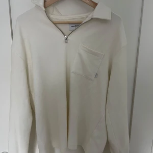 Vit tröja med dragkedja från Woodbird - Säljer en stilren vit tröja från Woodbird i storlek S. Tröjan har en praktisk dragkedja framtill och en bröstficka som ger en cool touch. Perfekt för både vardag och lite mer avslappnade tillfällen. Passar bra till jeans eller chinos!