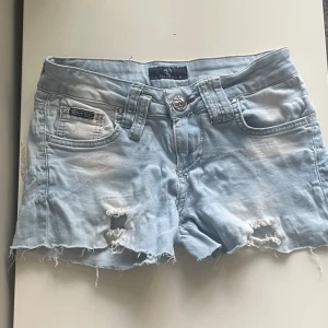 Ljusblå jeansshorts från Philipp Plein - Säljer ett par ljusblå jeansshorts från Philipp Plein. De har en cool slitning och  slitna kanter. Shortsen har en snygg dödskallebroderi på bakfickorna och en metalllogga på baksidan. STORLEK 27 MEN PASSAR XS💗