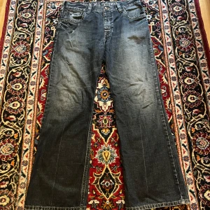 Baggy bootcut John Richmond jeans✨ - Skiiiitsnygga John Richmond bootcut jeans me cool distressing och snygga detaljer✨ Dom är blåare i verkligheten, vne varför dom ser så gråa ut på bilderna men oh well🤷‍♀️Dom har ganska mycket heelbite (som du kan se på bilderna) + lagade hål i fickorna❤️