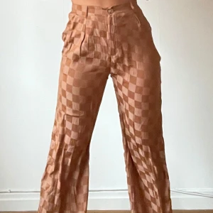 Bruna rutiga byxor - Säljer ett par snygga bruna byxor med rutigt mönster. De är högmidjade och har en loose passform som ger en avslappnad stil. Perfekta för både vardag och fest! 🧡