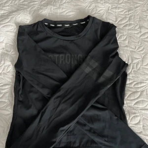 Svart långärmad tröja från Stronger - Säljer en svart långärmad tröja från Stronger. Den har en stilren design med texten 'STRONGER' tryckt på framsidan. Perfekt för träning eller en avslappnad dag. Materialet känns mjukt och bekvämt mot huden.