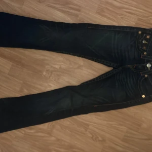 Mörkblå jeans från True Religion - Säljer ett par snygga mörkblå jeans från True Religion i storlek 23. De har en klassisk femficksdesign med coola detaljer på bakfickorna och en knappgylf. Perfekta för både vardag och fest! 🕺Avklippta, innersöm 71 cm, yttersöm 89 cm. Midja 32cm rakt över. Mycket fint skick!