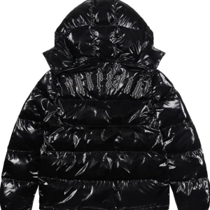 Svart glansig pufferjacka - Säljer en supercool svart glansig pufferjacka med huva. Jackan har en snygg dragkedja med ett unikt T-formad dragkedjehandtag och ett märke på bröstet med texten 'Trapstar'. Perfekt för att hålla sig varm och stilren under vintern!