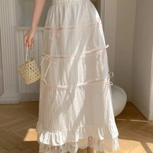 Vit långkjol med spetsdetaljer - Superfin vit långkjol med romantiska spetsdetaljer längst ner. Kjolen har en volangkant och söta knytband som ger en extra touch. Perfekt för sommarens alla fester eller en mysig dag på stan. Den är luftig och bekväm, vilket gör den idealisk för varma dagar.