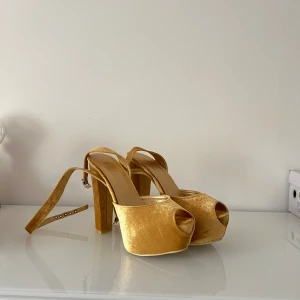 Guld klackar från NELLY - Helt oanvända Nelly klackar i perfekt skick. Velour material i guld utan några tecken på användning. Ser helt nya ut och har helt ren sula. Finns inte att köpa längre och har 14cm klack😍❤️