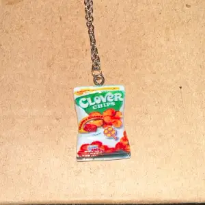 Unikt halsband med en rolig och färgglad Clover Chips-berlock. Perfekt för dig som vill ha något annorlunda och lekfullt i din smyckessamling. Kedjan är i silverfärg och berlocken ser ut som en liten chipspåse med detaljer i grönt, vitt och rött.