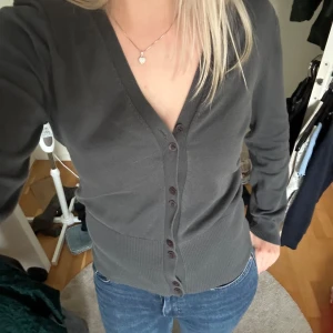 Grå kofta med knappar - Säljer en stilren och bekväm grå kofta med knappar framtill. Den har en v-ringad design och långa ärmar, perfekt för både vardag och lite kyligare dagar. Koftan är i bra skick och passar till det mesta i garderoben. Perfekt för höst och vår!