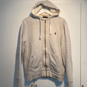 Polo Ralph Lauren Zip-Hoodie  - Polo Ralph Lauren Zip-Hoodie i ljusgrå. Produceras ej längre. Nypris 1900kr. Enormt bra basplagg, passar till allt från skjorta till t-shirt, stilsäker & ikonisk. Storlek M. Välanvänd men i dugligt skick. Pris kan diskuteras. Hörs i DM! 