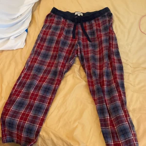 Pjamasbyxor - Säljer ett par superbekväma och stiliga pjamas byxor från Kappahl. De är i storlek L och har en snygg kombination av rött och blått i mönstret. Perfekta för en avslappnad dag hemma eller som mysbyxor. De har en elastisk midja med snörning för bästa 