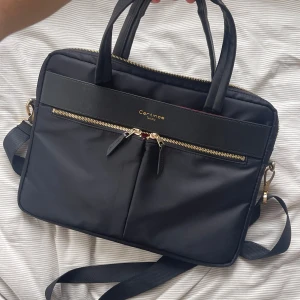 Datorväska - Superfin datorväska jag aldrig använt. Den rymmer mycket plats och har axelrem som går att ta av samt hållband beroende på preferens. Guld, svart och röd med fickor på sidan. TOPPSKICK