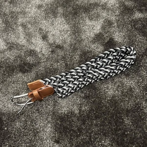 Flätat bälte med läderdetaljer - Säljer ett snyggt flätat bälte i svart och vitt med bruna läderdetaljer. Bältet har en klassisk design med en silverfärgad spänne. Perfekt för både vardag och fest!