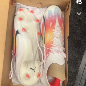 Färgglada fotbollsskor från Puma - Säljer ett par riktigt snygga fotbollsskor från Puma. De har en cool färgkombination av vit, röd, orange och blå med ett häftigt mönster. Skorna har snörning och är perfekta för fotbollsspel på gräs. Sulan har röda dobbar för extra grepp.