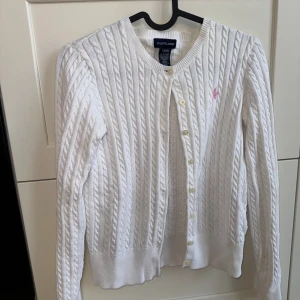 Vit Kabelstickad Kofta med rosa häst från Ralph Lauren - Kabelstickad kofta från Ralph Lauren. Barnstorlek men funkar till XS dam