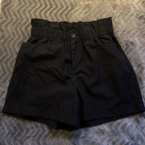 Svarta shorts med hög midja - Säljer ett par snygga svarta shorts med hög midja från Reserved. De har en bekväm passform. Shortsen har en knapp framtill och en praktisk bakficka. Perfekta för sommardagar! 🌟
