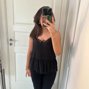 Svart ärmlös topp med spetsdetaljer - Säljer en snygg svart topp med spetsdetaljer vid halsringningen. Den har som vågigt material och är väldigt skön och luftig. Passar perfekt till fest!💖