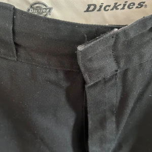 Svarta byxor från Dickies - Säljer ett par svarta byxor från Dickies. De har rak passform. Perfekta för både vardag och lite mer uppklädda tillfällen. Byxorna har dragkedja och knapp framtill. Modellen heter elizaville! 