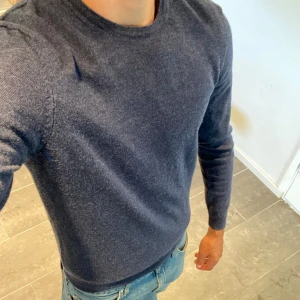 Mörkblå tröja merinoull  - Säljer en snygg och bekväm mörkblå merino ull tröja från Hugo boss. Tröjan har en klassisk rund hals och långa ärmar. Perfekt för höst och vinter, den är både stilren och varm. Passar bra till både jeans och chinos. Använd men i fint skick!