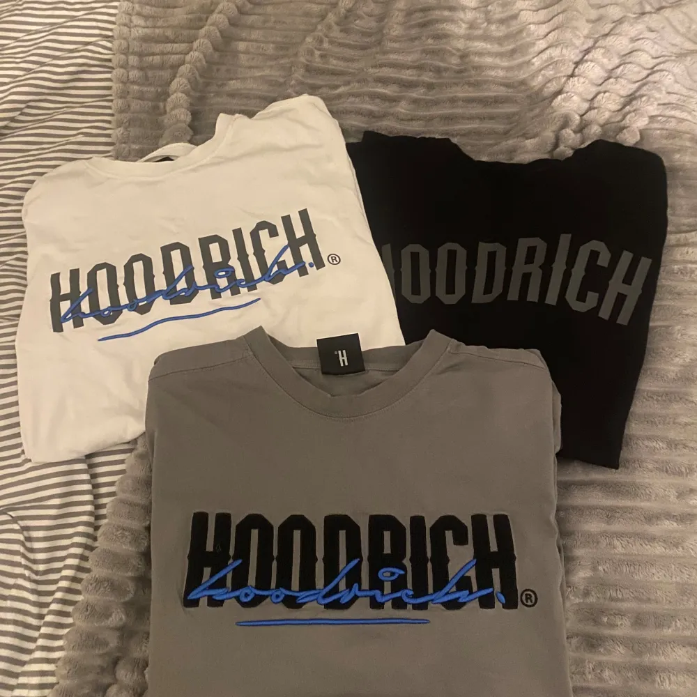 Säljer tre snygga t-shirts från Hoodrich i färgerna vit, svart och grå. Alla har en stor logga på framsidan i svart och blått. Perfekta för en casual look och passar till alla tillfällen!. T-shirts.