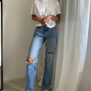 Blå jeans med slitningar - Säljer ett par snygga blå jeans med slitningar/håll på knäna. Jeansen är straight, High Waist från Gina tricket och i bra skick. Skriv om fler bilder önskas:)