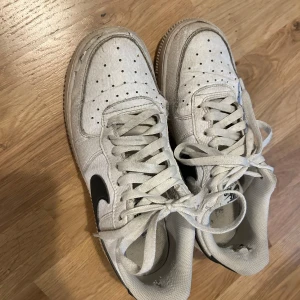 Vita Nike sneakers med svart swoosh - Säljer ett par vita Nike sneakers med svart swoosh. De är lite slitna men fortfarande snygga och bekväma. Perfekta för vardagsbruk. 