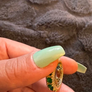 Guldring med gröna stenar - Säljer en äkta silver snygg guldring med gröna stenar. Ringen har en elegant design med rektangulära gröna stenar som är inramade av små glittriga stenar. Perfekt för att lägga till en touch av glamour till din outfit!
