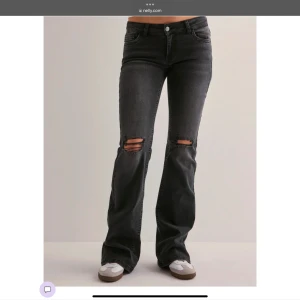 Svarta bootcut jeans med slitningar - Snygga svarta bootcut low wasted jeans med slitningar på knäna. De har en klassisk femficksdesign och knappar i midjan. Perfekta för en avslappnad stil med en touch av edge. Aldrig and vända