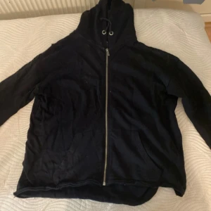 Svart hoodie med dragkedja - Säljer en svart hoodie med dragkedja och huva. Den har långa ärmar och en praktisk ficka framtill. Perfekt för en avslappnad stil.