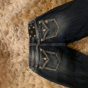 super söta ultra lowrise MissMe jeans - Snygga blå jeans från Miss Me med coola nitar och broderade detaljer. De är tyvärr för små för mig, så kan inte visa de på. De är helt riktiga och i supererbra skick! De är endast provade. I storlek 27, men skulle även passa en 28/29. Pris är väldigt diskuterbart