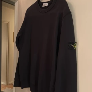 Svart tröja från Stone Island Junior - Snygg svart tröja från Stone Island Junior med deras ikoniska märke på ärmen. Tröjan har en rund hals och långa ärmar, perfekt för en stilren look.  Tröjan är använd men i väldigt bra skick då jag växte ur den väldigt snabbt. Tröjan är i storlek xl för junior och köptes på nk barn avdelning.