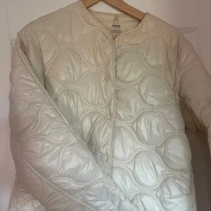 Vit quiltad jacka från MNG - Säljer en snygg vit quiltad jacka från MNG. Jackan har en rund hals och knäpps med knappar framtill. Den är perfekt för vår och höst och har en normal passform. 