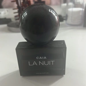 CAIA La Nuit Eau de Parfum - Elegant parfymflaska från CAIA med namnet La Nuit. Flaskan är mörk och fyrkantig med en stor, rund svart kork. Perfekt för den som söker en ny doft. 