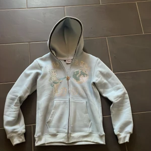 Rhinestone hoodie - Säljer en ljusblå hoodie från aim for the moon  med glittrigt tryck av en figur och texten 'Fly to the Moon'. Perfekt till våren/sommaren. Pris går att diskuter 🪐✨